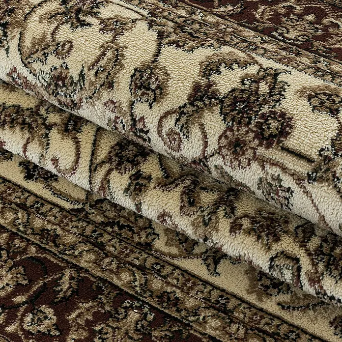 Kurzflorteppich Kashmir 2604Cream, 150 x 80 cm, 100% Polypropylen - Nahaufnahme eines gerollten Teppichs mit beigem Hintergrund und braunen floralen Mustern.