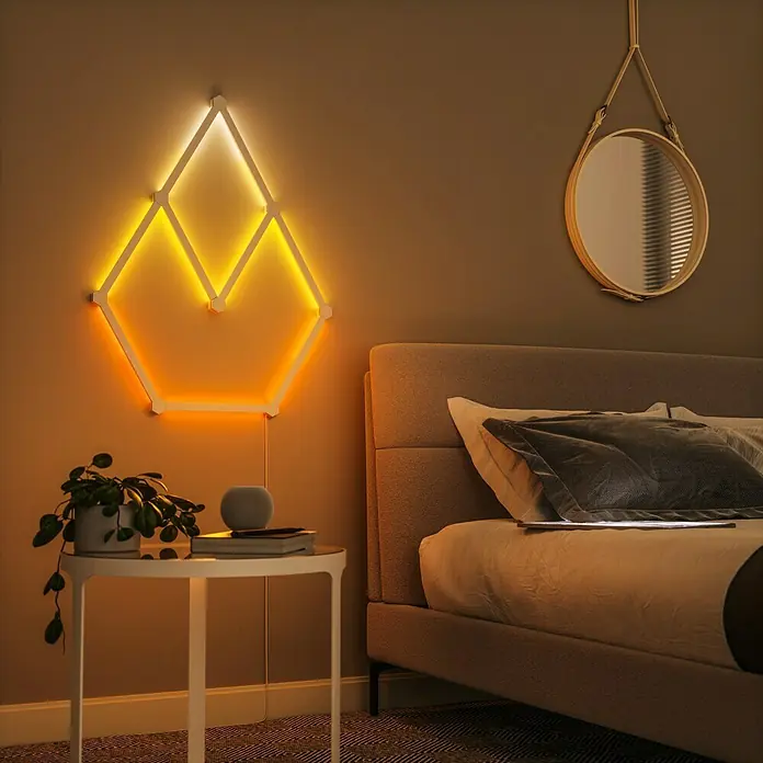 Nanoleaf Erweiterungskit Lines 60 Degrees 3 Lines - 3 Stk., Weiß, RGBW - Ein stilvolles Schlafzimmer mit einem modernen Nachttisch und einer geometrischen LED-Wandleuchte, die ein warmes Licht ausstrahlt.