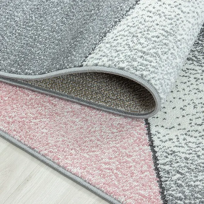 Kurzflorteppich Beta 1120Pink, 150 x 80 cm, 100 % Polypropylen - Nahaufnahme eines geometrischen Teppichs in Rosa, Grau und Weiß, dessen Ecke aufgerollt ist.