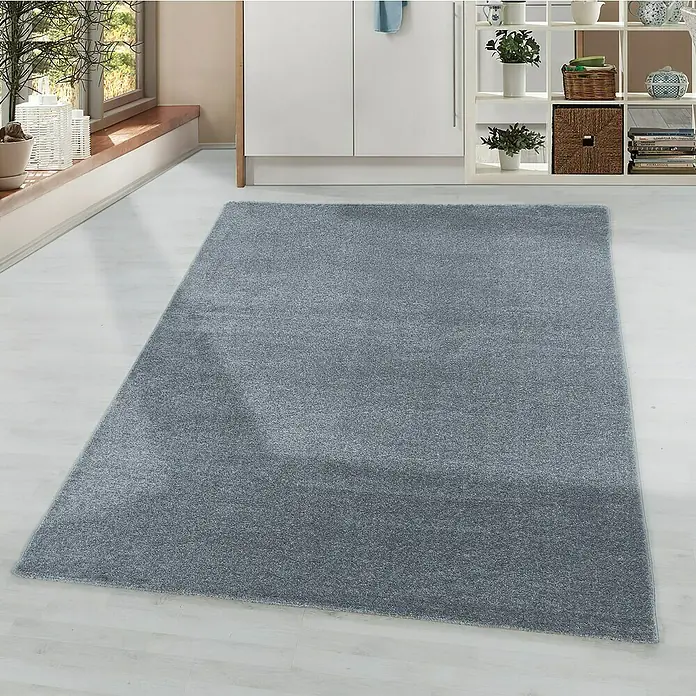 Hochflorteppich Rio 4600 - Silber, 150 x 80 cm, 100% Polypropylen - Ein grauer Teppich liegt auf einem hellen Holzboden vor einem weißen Schrank und einem Regal. Der Teppich hat eine weiche, flauschige Textur.