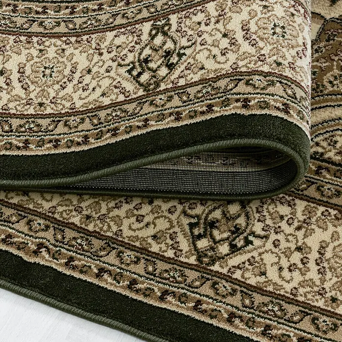 Kurzflorteppich Kashmir 2601Grün, 290 x 200 cm, 100% Polypropylen - Nahaufnahme eines beigefarbenen Teppichs mit einem grünen Rand, der teilweise aufgerollt ist. Das Muster ist klassisch und detailreich.
