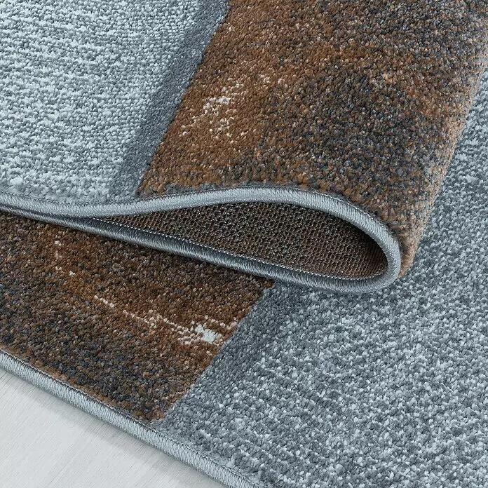 Kurzflorteppich Ottawa 4201 - Kupfer, 200 x 140 cm, 100% Polypropylen - Texturierter Teppich in Grau und Braun, teilweise gefaltet, zeigt seinen weichen Flor und Kante auf hellem Holzboden.
