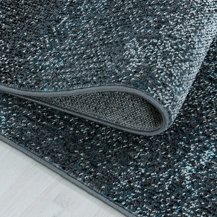 Kurzflorteppich Ottawa 4203 - Blau, 150 x 80 cm, 100% Polypropylen - Detailaufnahme eines grauen Teppichs mit Muster, der aufgerollt ist und seine Textur und Farbe zeigt.