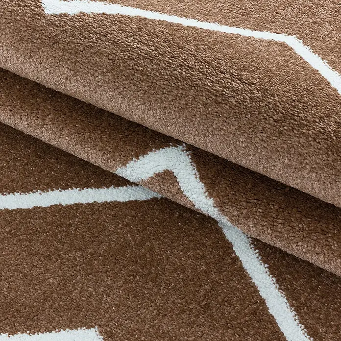 Hochflorteppich Rio 4602Kupfer, 200 x 140 cm, 100% Polypropylen - Detailansicht eines braunen Teppichs mit weißem geometrischen Muster. Das Textil weist eine weiche, plüschartige Textur auf.