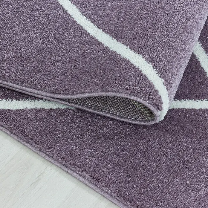 Hochflorteppich Rio 4601Lila, 150 x 80 cm, 100% Polypropylen - Nahaufnahme eines lila Teppichs mit weißem geometrischem Muster, der eine weiche und bequeme Textur zeigt.