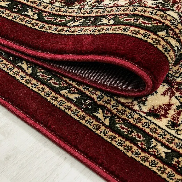 Kurzflorteppich Orient-Optik Marrakesh 0297 - Rot, 290 x 200 cm, 100% Polypropylen - Detailaufnahme eines roten Teppichs mit traditionellem Muster und umgeschlagenem Rand, der die Unterseite zeigt.