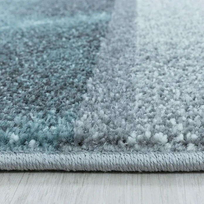 Kurzflorteppich Ottawa 4201 - Blau, 200 x 140 cm, 100% Polypropylen - Nahaufnahme eines Teppichs mit blau-grauem Farbverlauf und gekettelten Rändern, der eine weiche Textur und hochwertige Verarbeitung zeigt.