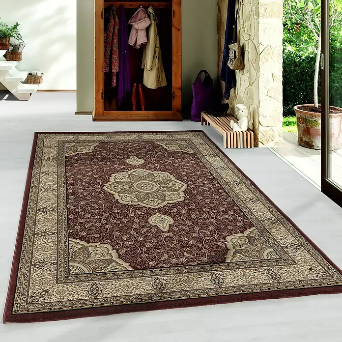 Kurzflorteppich Kashmir 2601Rot, 150 x 80 cm, 100% Polypropylen - Ein detailreicher, brauner Teppich mit floralen Mustern liegt in einem hellen Flur und verleiht dem Raum Wärme und Eleganz.