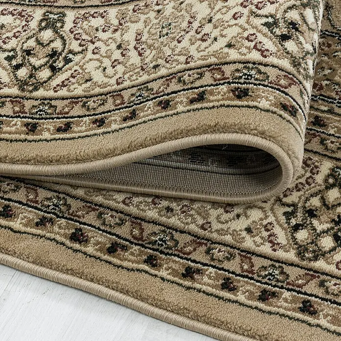 Kurzflorteppich Kashmir 2601Beige, 150 x 80 cm, 100% Polypropylen - Detailansicht eines beigefarbenen Teppichs mit floralem Muster und gerolltem Rand, der die Textur und Verarbeitung hervorhebt.