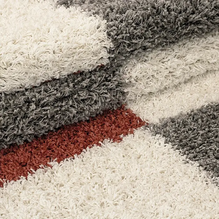 Hochflorteppich Gala 2505Terra, 110 x 60 cm, 100% Polypropylen - Nahaufnahme eines Teppichs mit weißen, grauen und roten Streifen, der eine weiche Textur und ein modernes Design aufweist.