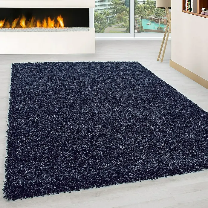 Hochflorteppich Life 1500Navy, 200 x 100 cm, 100% Polypropylen - Ein dunkelblauer, rechteckiger Shaggy-Teppich liegt auf einem hellen Holzboden vor einem modernen Kamin. Der Teppich hat eine dichte, flauschige Textur.