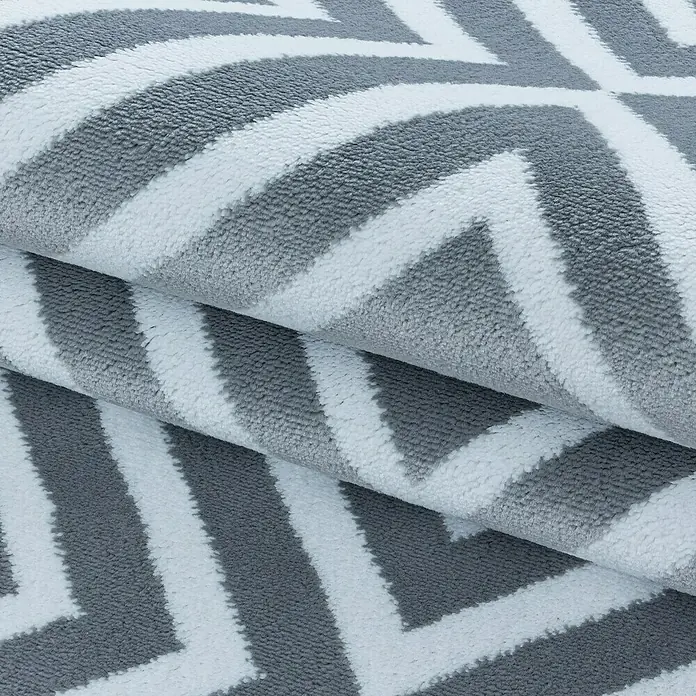 Kurzflorteppich Costa 3525 - Grau, 250 x 80 cm, 100 % Polypropylen - Nahaufnahme eines gefalteten Teppichs mit grau-weißem Zickzackmuster, der Textur und Design hervorhebt. Ideal für moderne Dekore.