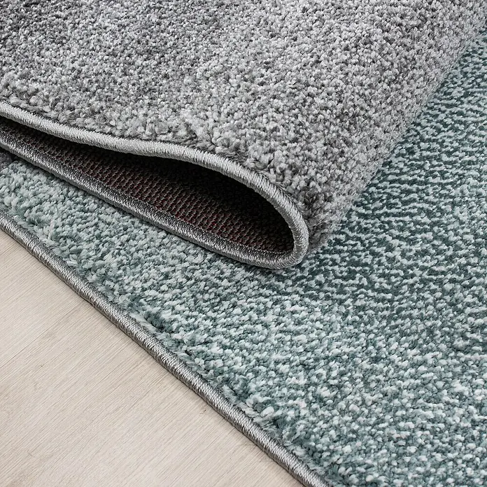Kurzflorteppich Lucca 1810 - Blau, 150 x 80 cm, 100% Polypropylen - Nahaufnahme eines grauen und blauen Teppichs mit Textur und Bordüre, der die Detailgenauigkeit und Verarbeitung des Produkts hervorhebt.