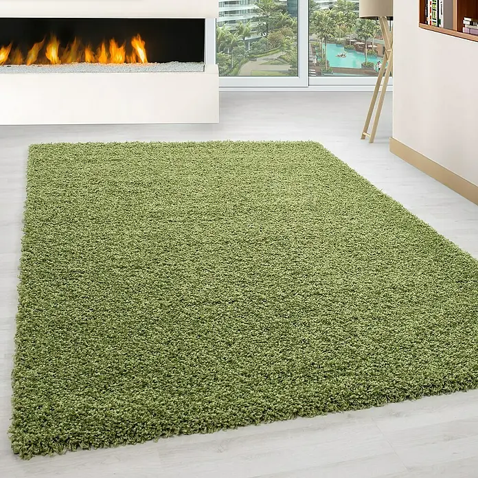 Hochflorteppich Life 1500Grün, 250 x 80 cm, 100% Polypropylen - Ein grüner, hochfloriger Teppich liegt in einem modernen Wohnzimmer mit Kamin und Fensterfront. Der Teppich sorgt für eine gemütliche Atmosphäre.