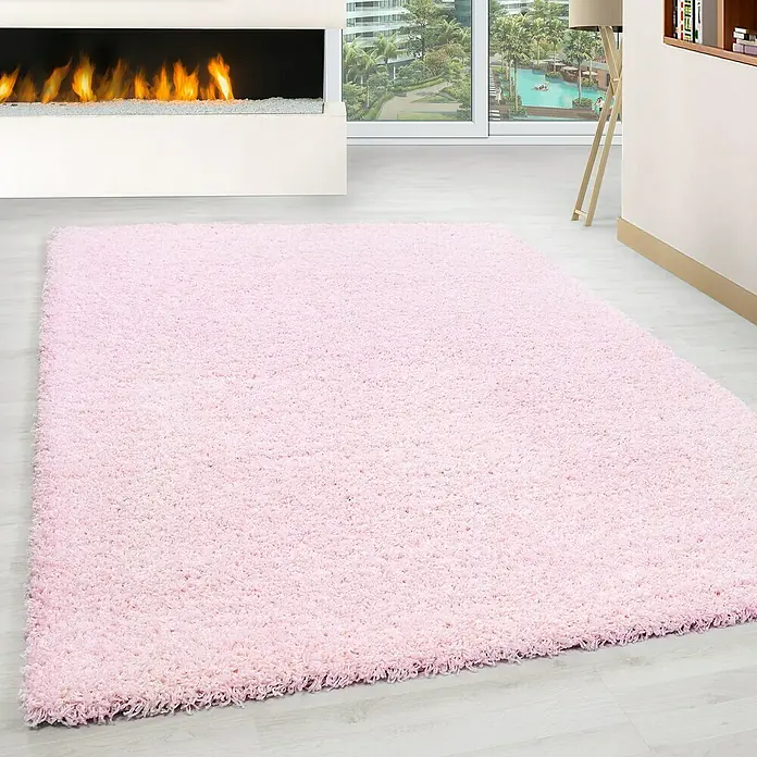Hochflorteppich Life 1500Pink, 400 x 300 cm, 100% Polypropylen - Ein weicher, rosa Shaggy-Teppich liegt in einem hellen Wohnzimmer mit Kamin und Blick nach draußen. Der Teppich sorgt für Wärme und Komfort.