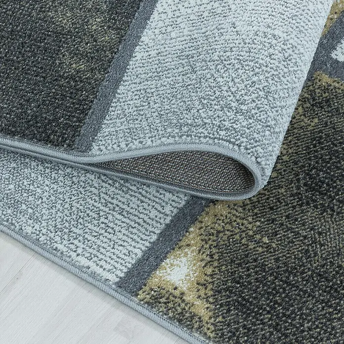 Kurzflorteppich Ottawa 4201 - Gelb, 150 x 80 cm, 100% Polypropylen - Detailaufnahme eines modernen Teppichs mit geometrischem Muster in Grau- und Brauntönen, teilweise aufgerollt, der die Textur hervorhebt.