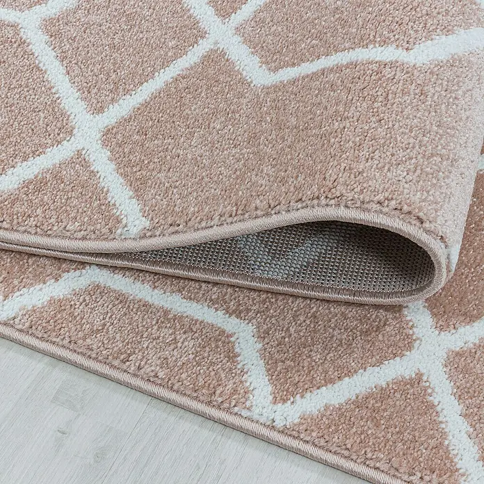 Kurzflorteppich Efor 3713Rose, 290 x 200 cm, 100% Polypropylen - Detailaufnahme eines beigen Teppichs mit geometrischem Muster. Der Teppich hat eine leicht aufgerollte Kante, die die Unterseite zeigt.