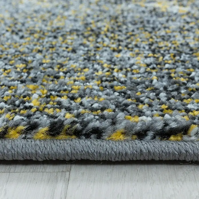 Kurzflorteppich Ottawa 4203 - Gelb, 150 x 80 cm, 100 % Polypropylen - Nahaufnahme eines Teppichs mit grauen, weißen, gelben und schwarzen Fasern. Der Teppich hat einen grauen Rand und liegt auf einem hellen Holzboden.