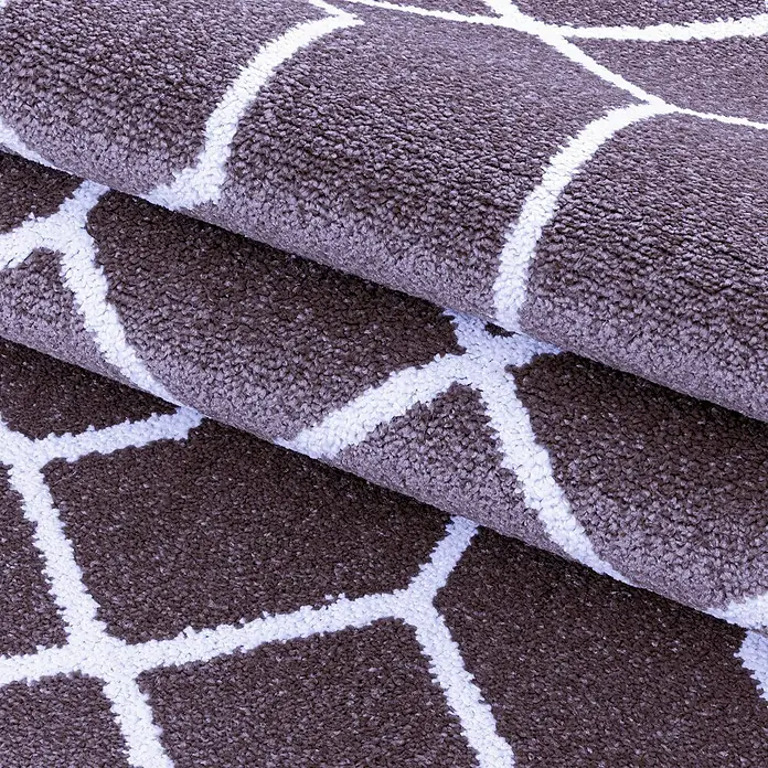 Kurzflorteppich Efor 3713Violett, 150 x 80 cm, 100 % Polypropylen - Detailaufnahme eines braunen Teppichs mit weißem, geometrischem Muster, der gefaltet ist.