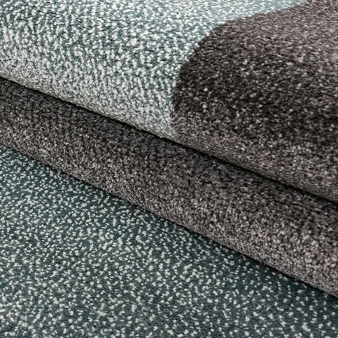 Kurzflorteppich Lucca 1810 - Blau, 150 x 80 cm, 100% Polypropylen - Nahaufnahme von Teppichrollen in verschiedenen Texturen und Farben, die die Materialqualität und Designvielfalt hervorheben.
