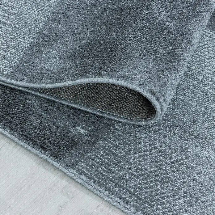 Kurzflorteppich Ottawa 4201 - Grau, 200 x 140 cm, 100% Polypropylen - Detailaufnahme eines grauen Teppichs mit gewebter Textur und umgeschlagenem Rand, der die Unterseite zeigt.