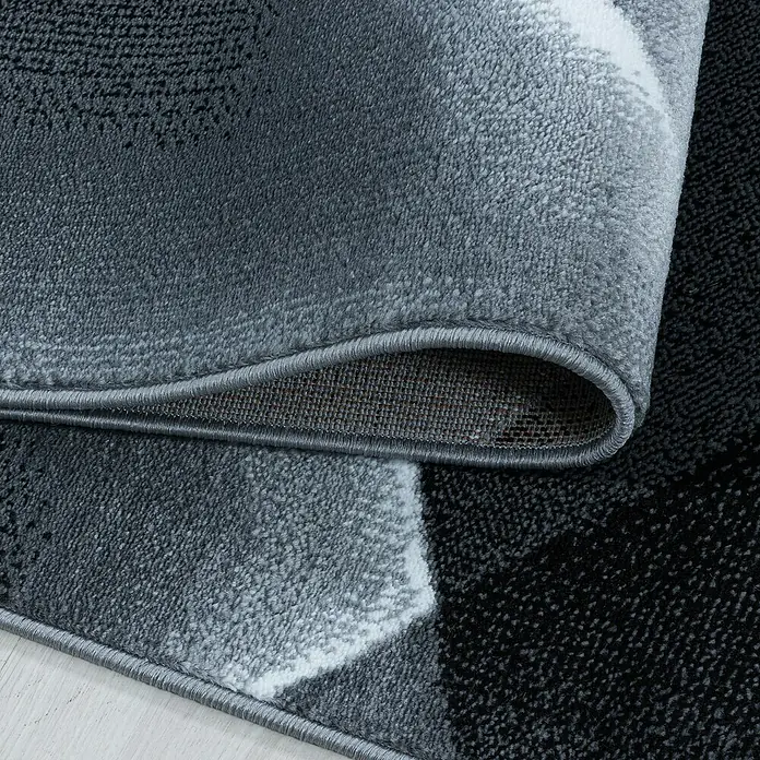 Kurzflorteppich Costa 3527Schwarz, 200 x 140 cm, 100% Polypropylen - Detailaufnahme eines modernen Teppichs in Grau- und Schwarztönen mit hochgezogener Ecke, die die Textur und Verarbeitung zeigt.
