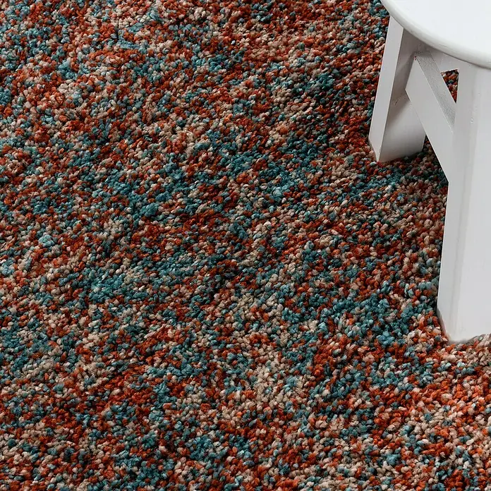 Hochflorteppich Enjoy 4500Terrakotta, 170 x 120 cm, 100 % Polypropylen - Nahaufnahme eines mehrfarbigen Teppichs mit einer weißen Tischbein im Bild.
