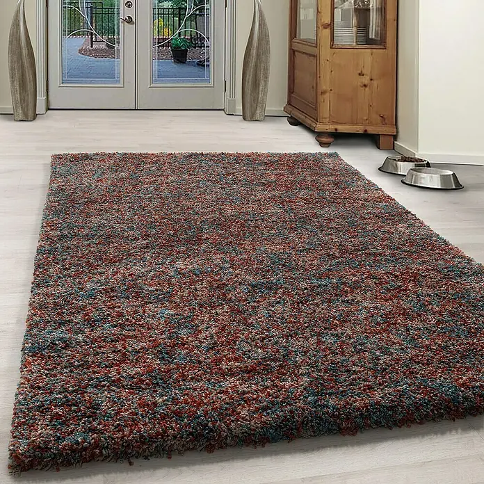 Hochflorteppich Enjoy 4500Terrakotta, 170 x 120 cm, 100 % Polypropylen - Bunter, mehrfarbiger Teppich im Raum vor einer Tür und einem Holzschrank.