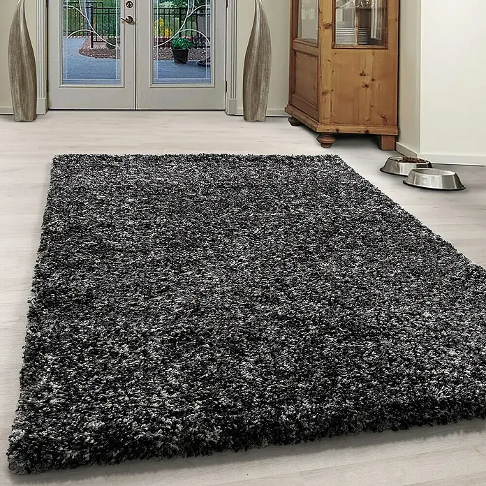 Hochflorteppich Enjoy 4500 - Anthrazit, 230 x 160 cm, 100 % Polypropylen - Ein grauer, zotteliger Teppich liegt in einem Raum mit Holzboden und einer Tür. Der Teppich verleiht dem Raum eine gemütliche Atmosphäre.