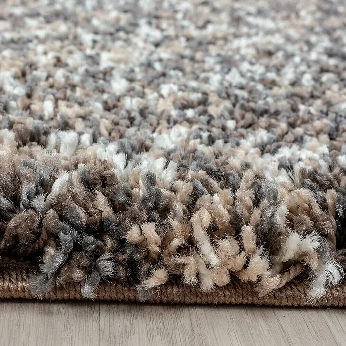 Hochflorteppich Enjoy 4500Taupe, 250 x 80 cm, 100 % Polypropylen - Nahaufnahme eines mehrfarbigen, zotteligen Teppichs mit braunen, grauen und weißen Fasern, der eine weiche und einladende Textur zeigt.
