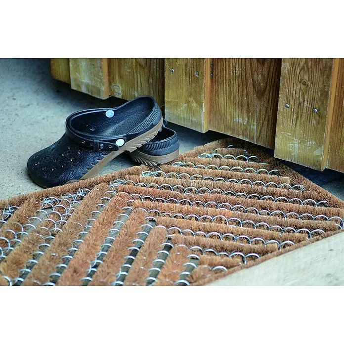 Astra Coco Fußmatte Brush - 40 x 60 cm, Kokos, Fischgrät - Braune Fußmatte aus Kokosfasern mit Metallringen und ein Paar schwarze Clogs. Ideal für den Eingangsbereich, um Schmutz abzufangen.