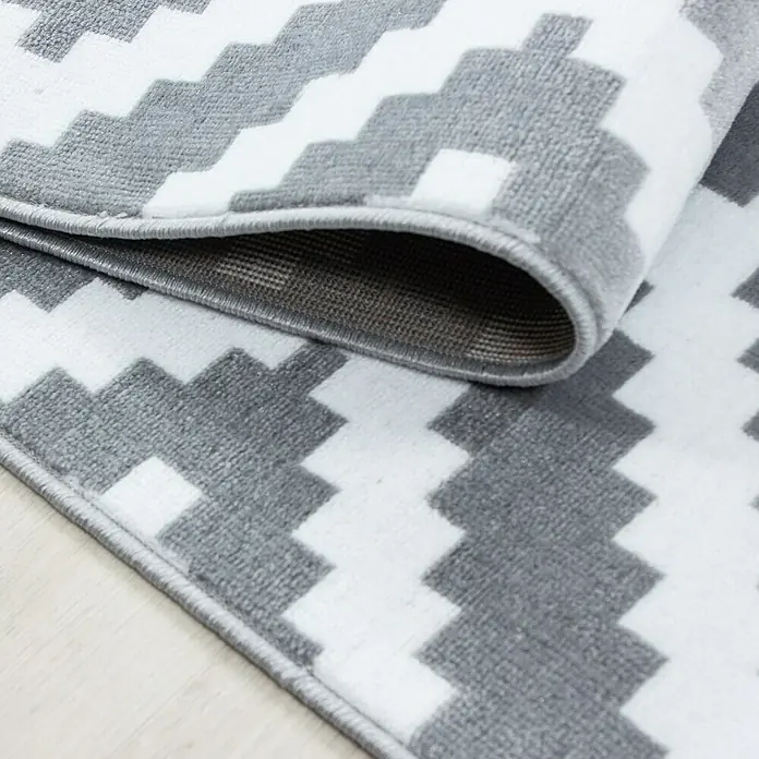 Kurzflorteppich Plus 8005Grau, 150 x 80 cm, 100% Polypropylen - Nahaufnahme eines Teppichs mit geometrischem Zickzackmuster in Grau und Weiß, der eine moderne Ästhetik für jeden Raum bietet.