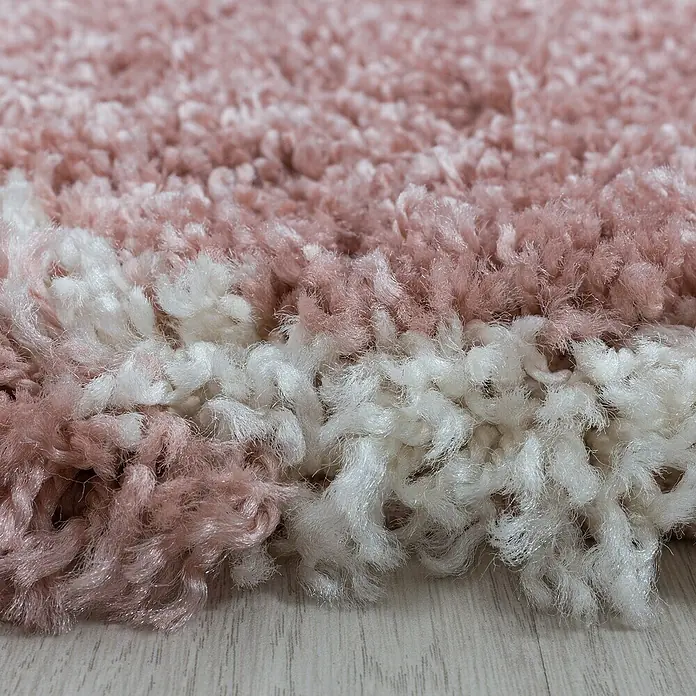 Hochflorteppich Salsa 3201Rose, Durchmesser: 160 cm, 100% Polypropylen - Nahaufnahme eines zotteligen Teppichs in Rosa und Weiß mit einer weichen, flauschigen Textur und einer hellen Holzoberfläche im Hintergrund.