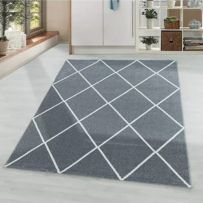 Hochflorteppich Rio 4601 - Silber, 150 x 80 cm, 100 % Polypropylen - Ein rechteckiger grauer Teppich mit weißen geometrischen Rautenmustern liegt auf hellem Holzboden in einem modernen Raum.