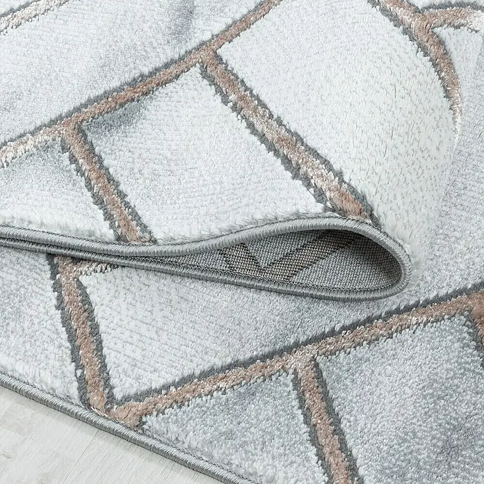 Kurzflorteppich Naxos 3813Bronze, 200 x 140 cm, 80% Polypropylen, 20% Polyester - Nahaufnahme eines stilvollen, hellen Teppichs mit modernem geometrischem Muster und aufgerolltem Rand, der die Textur zeigt.