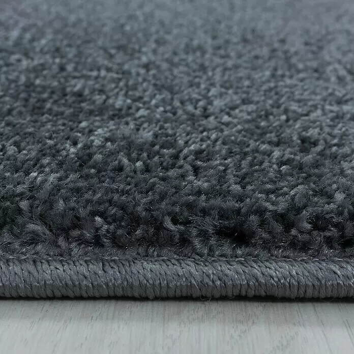 Hochflorteppich Rio 4600 - Grau, 150 x 80 cm, 100% Polypropylen - Nahaufnahme eines tiefgrauen, flauschigen Teppichs mit gewebter Kante auf hellem Holzfußboden.