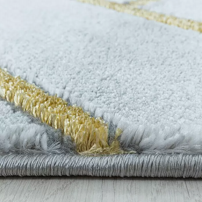 Kurzflorteppich Naxos 3813 - Gold, 200 x 140 cm, 80% Polypropylen, 20% Polyester - Nahaufnahme eines zotteligen Teppichs mit hellgrauen und gelben Fasern, Textur und sauber eingefasstem Rand auf hellem Holzboden.