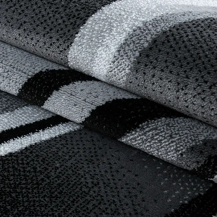 Kurzflorteppich Parma 9210 - Schwarz, 300 x 80 cm, 100% Polypropylen - Nahaufnahme eines Teppichs mit Streifenmuster in Grau-, Schwarz- und Weißtönen, der eine weiche und luxuriöse Textur aufweist.