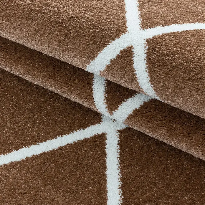 Hochflorteppich Rio 4601Kupfer, 230 x 160 cm, 100% Polypropylen - Nahaufnahme eines braunen Teppichs mit weißem geometrischem Muster, der eine weiche und moderne Textur zeigt.