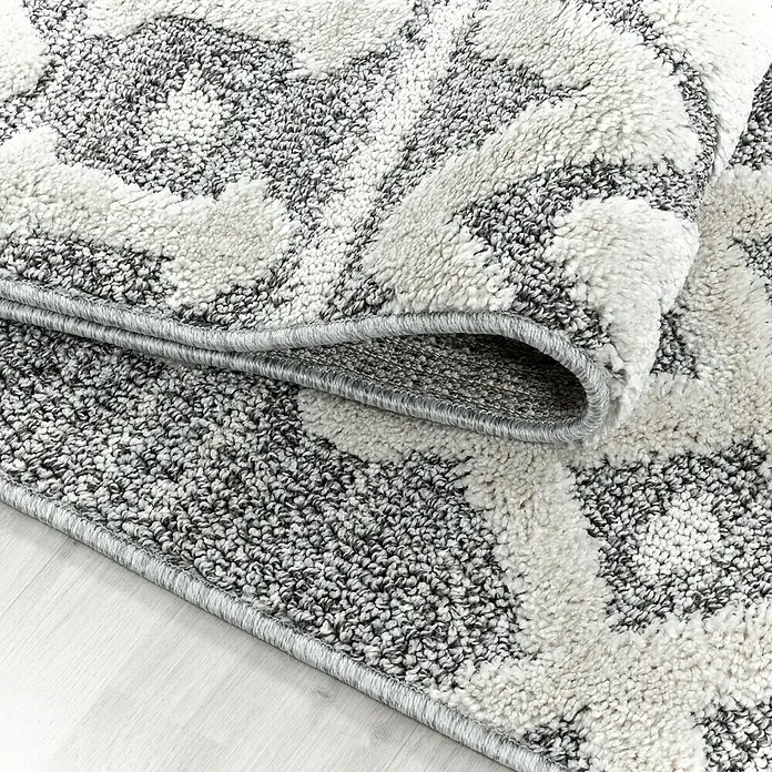 Hochflorteppich Pisa 4710Grau, 200 x 140 cm, 100 % Polypropylen - Detailaufnahme eines gemusterten Teppichs mit gerolltem Rand, der seine Textur und das graue Bordüre hervorhebt.