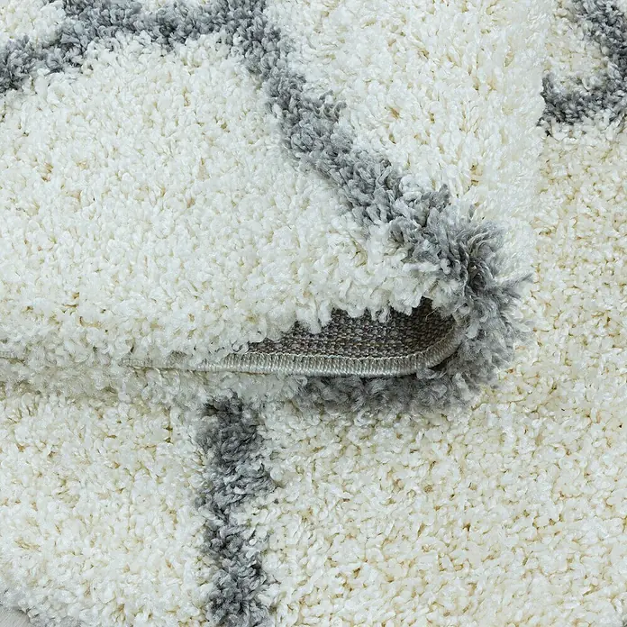 Hochflorteppich Salsa 3201 - Cream, 250 x 80 cm, 100% Polypropylen - Nahaufnahme eines weißen Teppichs mit grauem Muster und hochgeklappter Ecke, die die Unterseite zeigt. Weiche Textur und modernes Design.