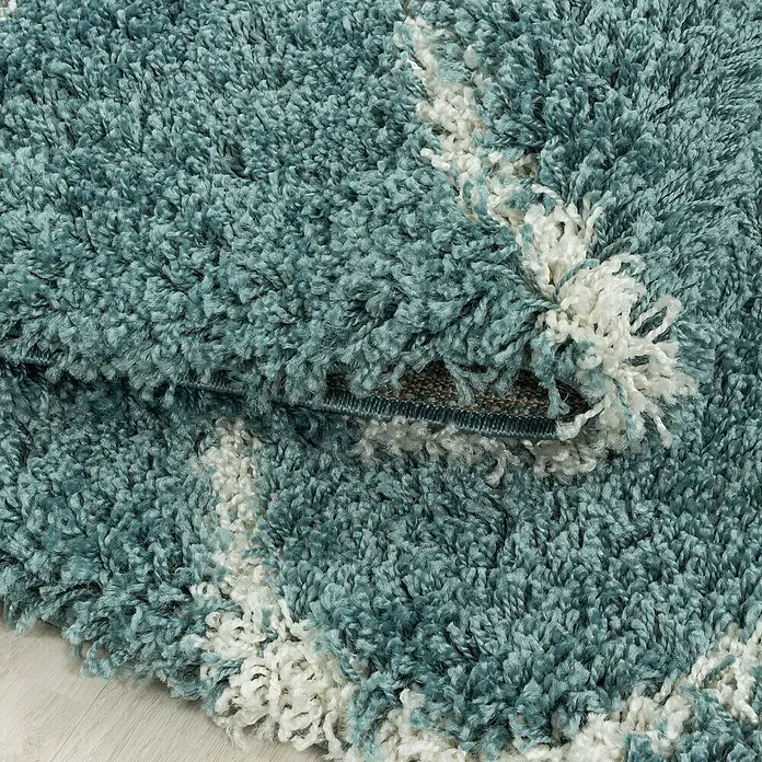 Hochflorteppich Salsa 3201Blau, 340 x 240 cm, 100% Polypropylen - Nahaufnahme eines blauen Shaggy-Teppichs mit weißen Akzenten und aufgerolltem Rand, der die Textur und Details hervorhebt.