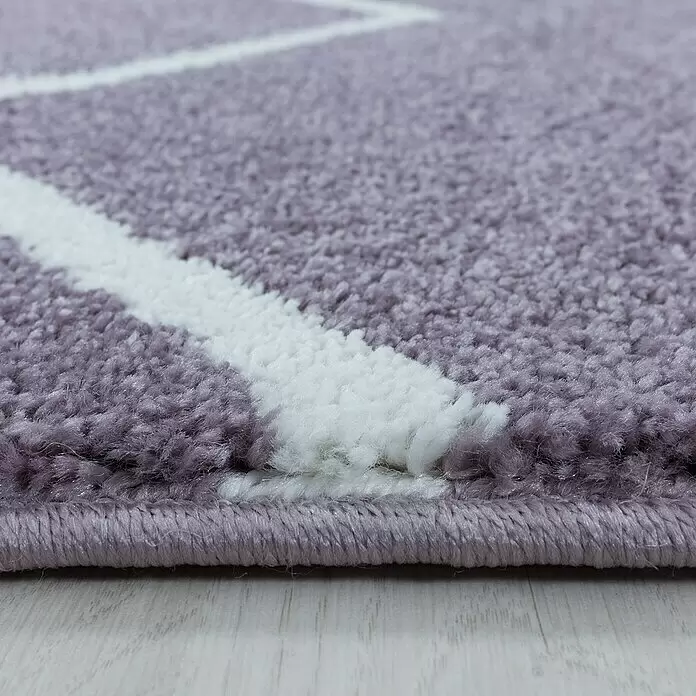Hochflorteppich Rio 4602 - Lila, 250 x 80 cm, 100% Polypropylen - Nahaufnahme eines weichen, fliederfarbenen Hochflorteppichs mit weißen geometrischen Mustern, der die plüschige Textur und den genähten Rand zeigt.