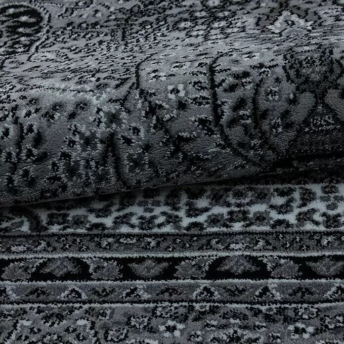 Kurzflorteppich Orient-Optik Marrakesh 0207 - Grau, 340 x 240 cm, 100% Polypropylen - Nahaufnahme eines gefalteten grauen Teppichs mit aufwendigen schwarz-weiß-grauen Mustern, die seine weiche Textur hervorheben.