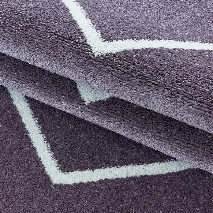 Hochflorteppich Rio 4602 - Lila, 250 x 80 cm, 100% Polypropylen - Nahaufnahme eines gefalteten, plüschigen lilafarbenen Teppichs mit weißem geometrischem Muster, der seine weiche Textur zeigt.