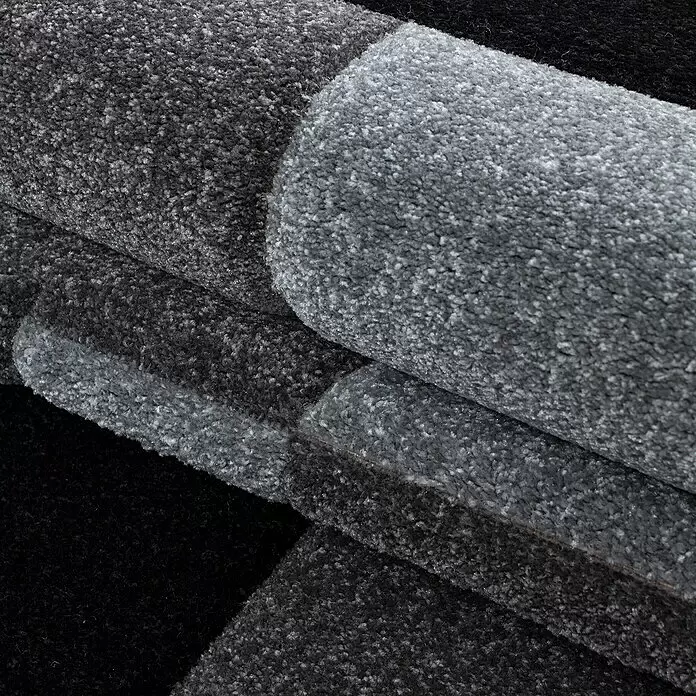 Kurzflorteppich Hawaii 1310 - Grau, 370 x 280 cm, 100 % Polypropylen - Gestapelte Rollen weicher, texturierter Teppiche in verschiedenen Grau- und Schwarztönen, die ihren Plüschflor zeigen.