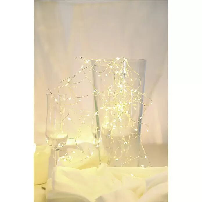 Globo LED-Lichterkette Venuto - Innen, Kabellänge: 9,9 m, Silber Metallic - Warmweiße LED-Lichterkette dekorativ um eine klare Glasvase, ein Sektglas und eine Kerze drapiert, erzeugt eine gemütliche Atmosphäre.