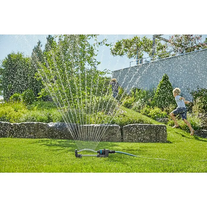 Gardena EcoLine ViereckregnerMax. Regnerfläche: 220 m² - Der Gardena Regner im Einsatz, während Kinder im Hintergrund spielen. Perfekt für die Bewässerung und den Spaß im Garten.