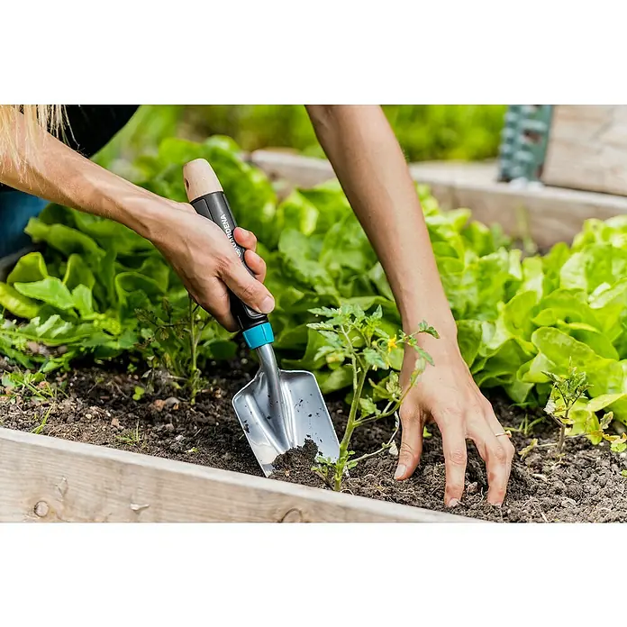 Gardena EcoLine Blumenkelle - Arbeitsbreite: 8,5 cm - Nahaufnahme einer Hand, die mit einer Gardena Pflanzkelle ein kleines Loch in einem Hochbeet für eine Jungpflanze macht.
