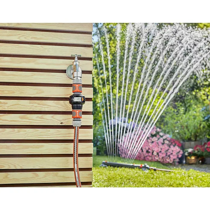 Gardena Wasserzähler AquaCount - Batteriebetrieben - Nahaufnahme des Gardena Wasserzählers am Wasserhahn, mit Beregnung im Hintergrund.